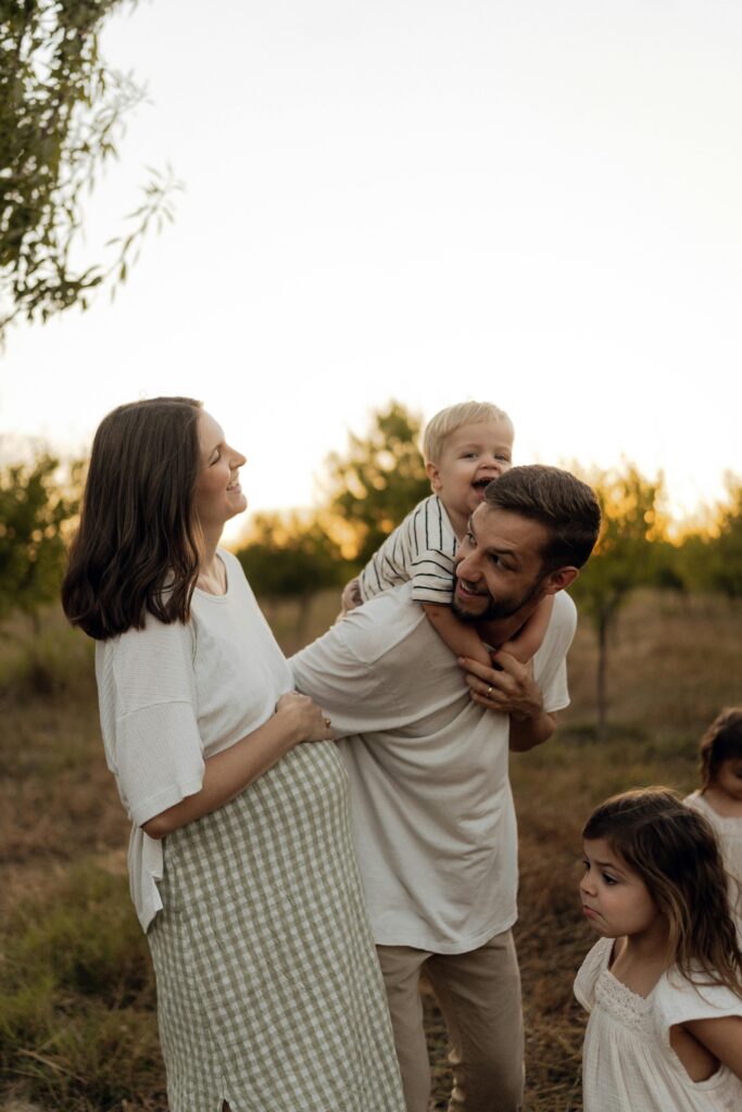A joyful family with children sharing a loving moment in a picturesque outdoor setting during sunset.