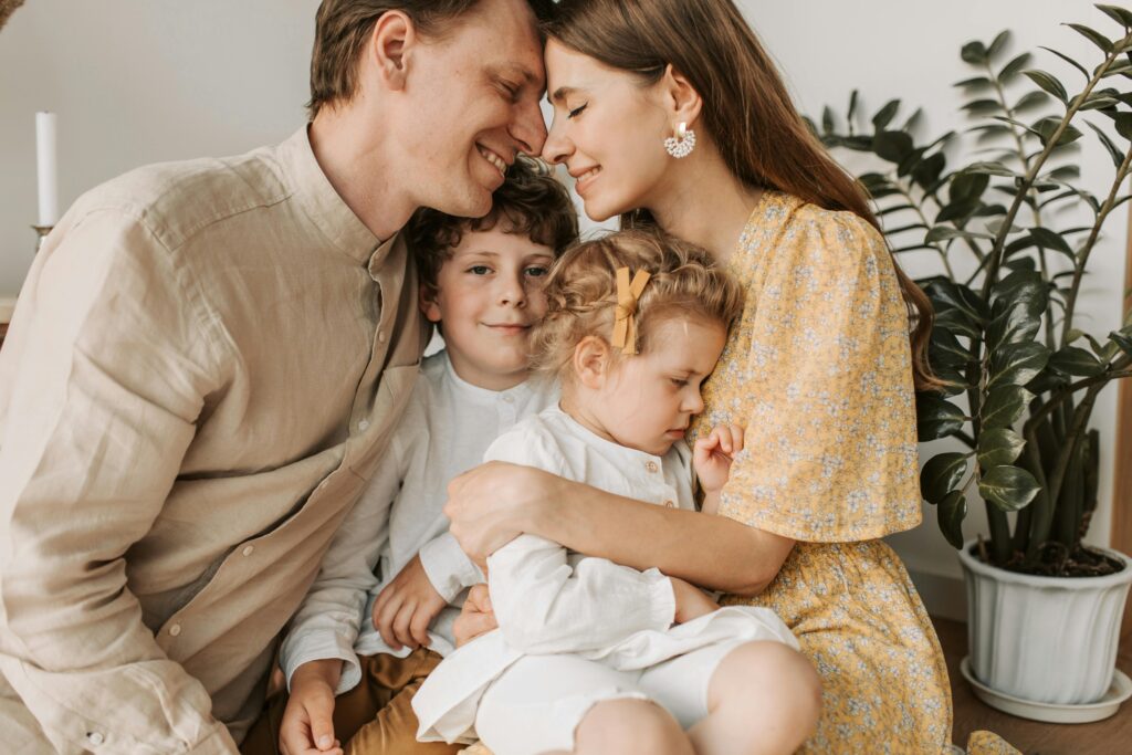 A loving family of four shares a tender moment in a cozy indoor setting, embracing and smiling.