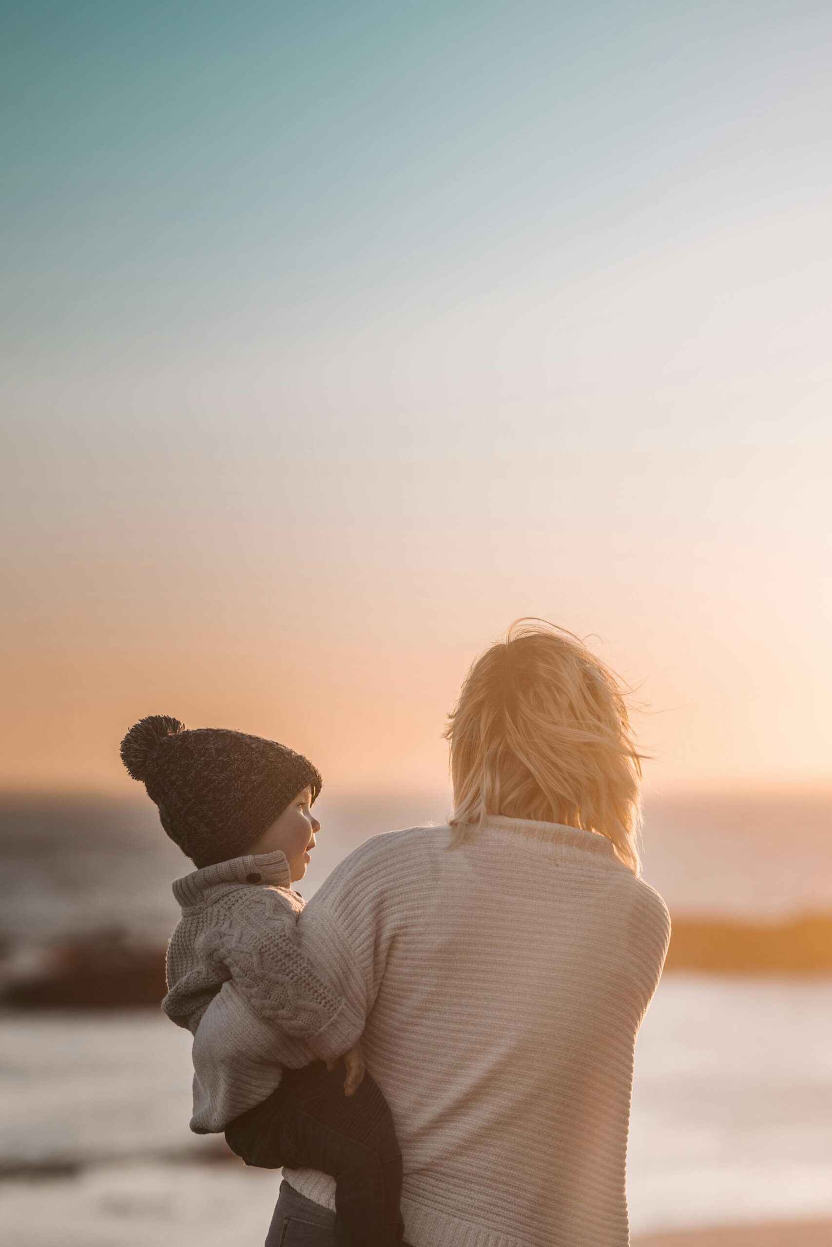 A mother and child share a tender moment on the beach during sunset.
